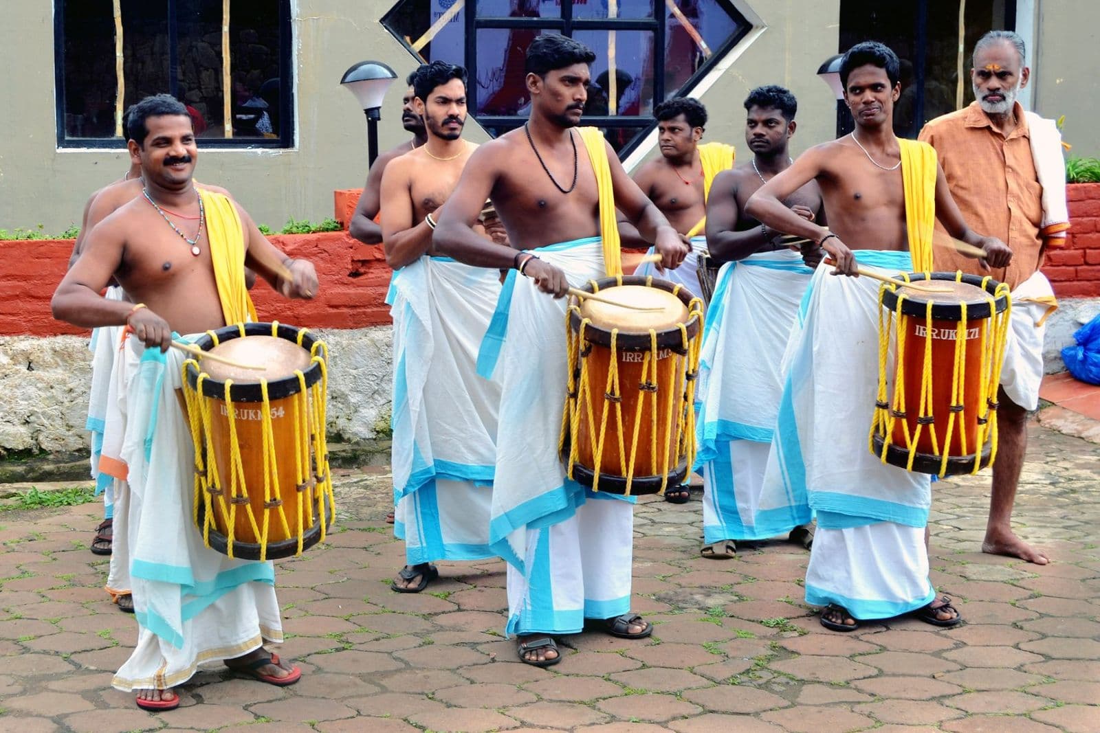 Chenda drummers in white mundus playing cylindrical drums at an outdoor function