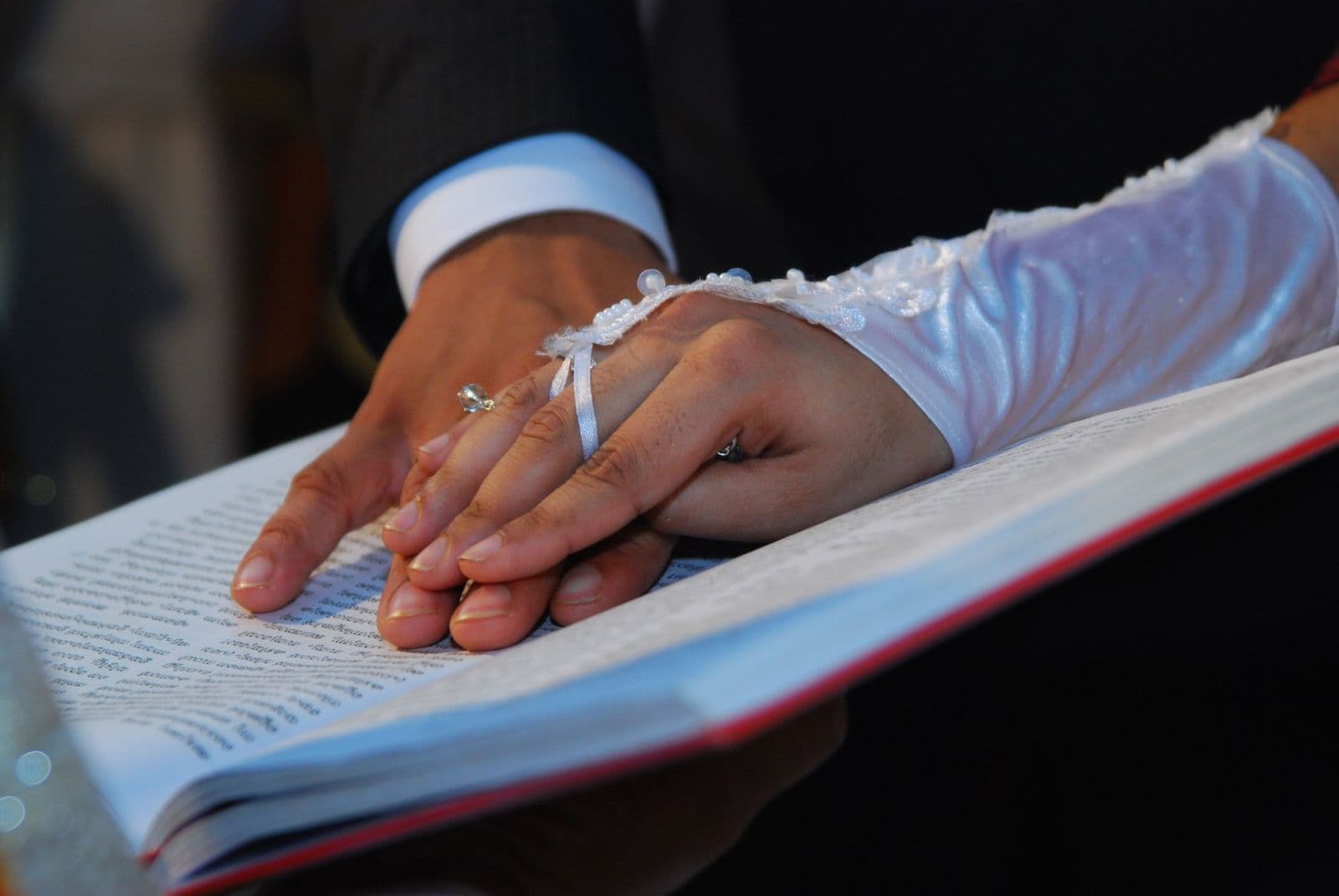 A bride's and groom's hands resting together on an open Bible during a Kerala Catholic wedding