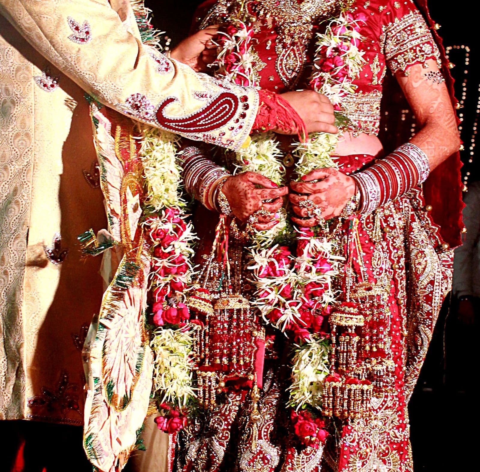 A bride and groom, seen from the shoulders down, holding heavy flower garlands before the garland exchange