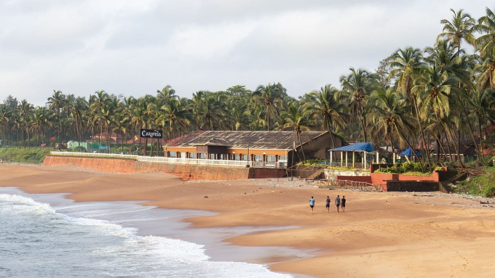 Sinquerim beach at sunset, with palms and low buildings behind the sand