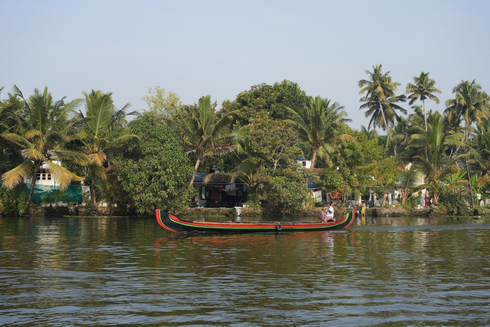 A canoe on still backwater lined with coconut palms and houses
