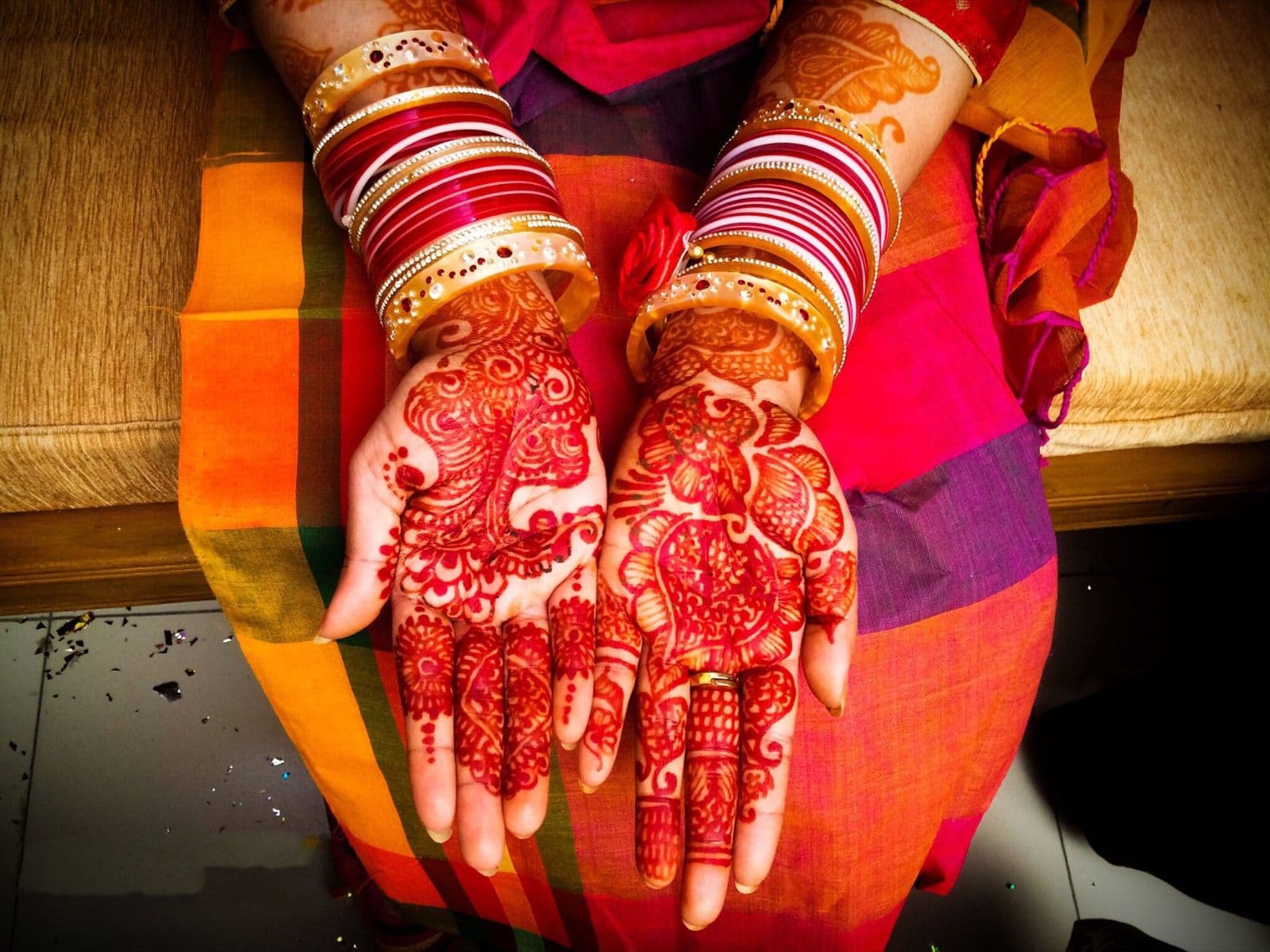 A bride's hands covered in fine red mehndi designs, with red and white bangles