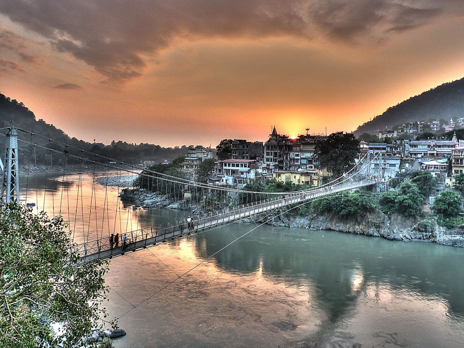 Lakshman Jhula and the temples of Rishikesh reflected in the Ganges under a glowing sunset