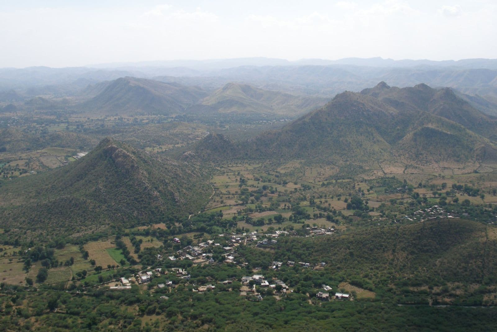 Green Aravalli hills and villages spreading out below a hazy sky outside Udaipur