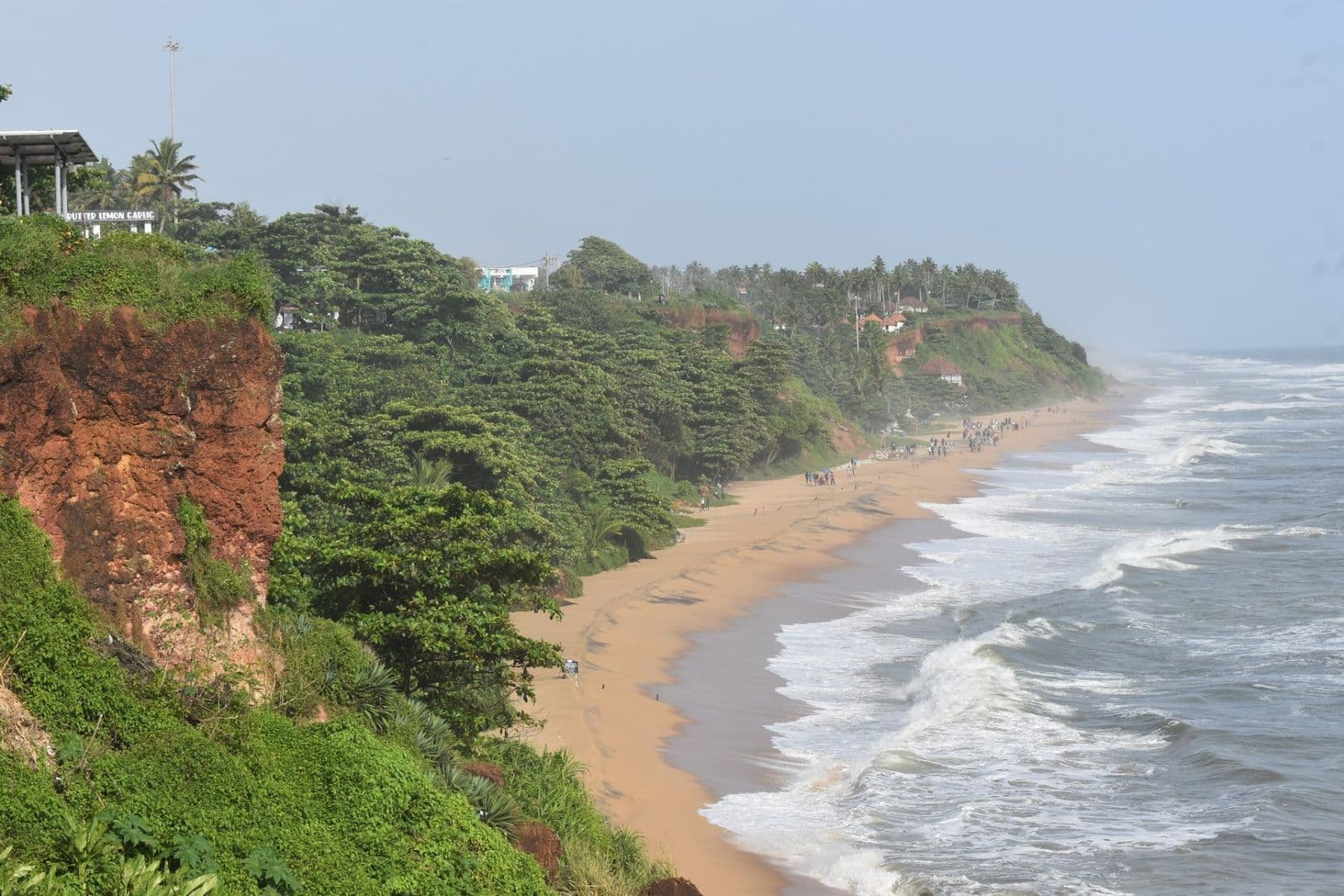 Red laterite cliffs and palms above a curving beach and white surf at Varkala